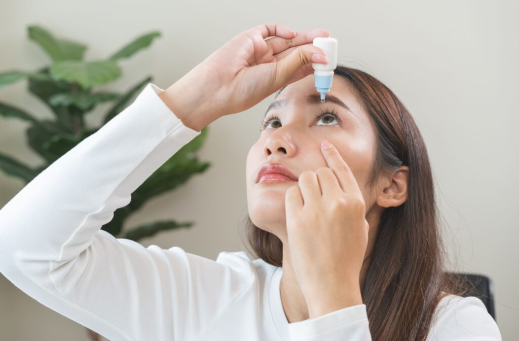 young asian woman applying eye drops directly into her eye.