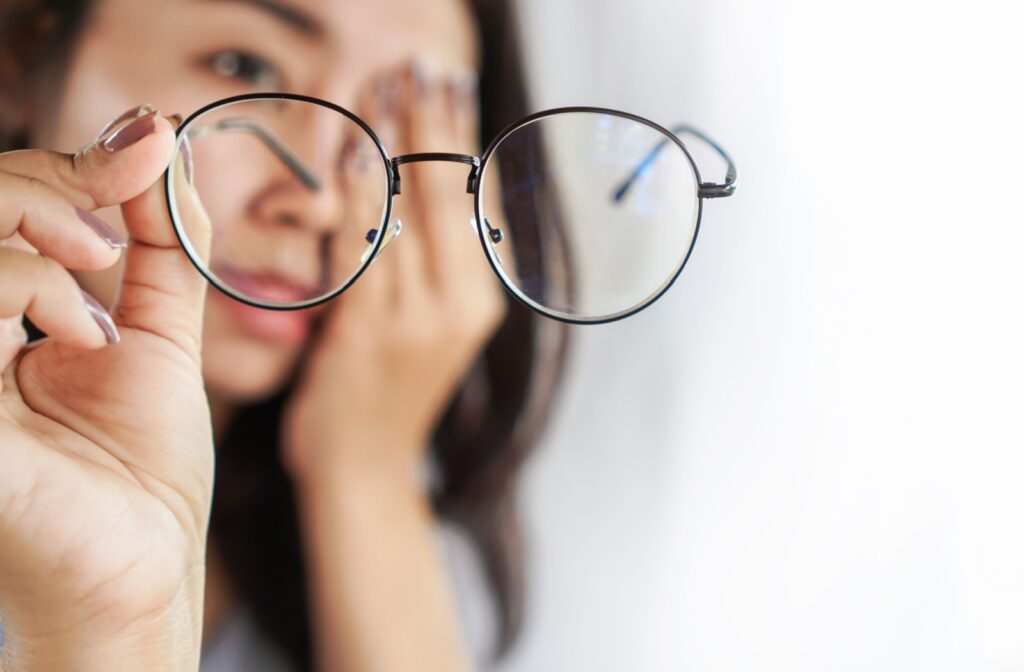 Woman holding blue light glasses, rubbing her tired eyes.