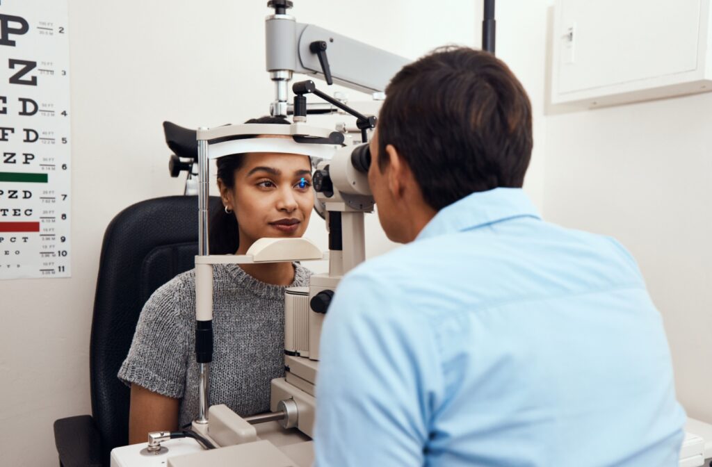 Optometrist using slit lamp to look into eye of female patient in grey sweater.