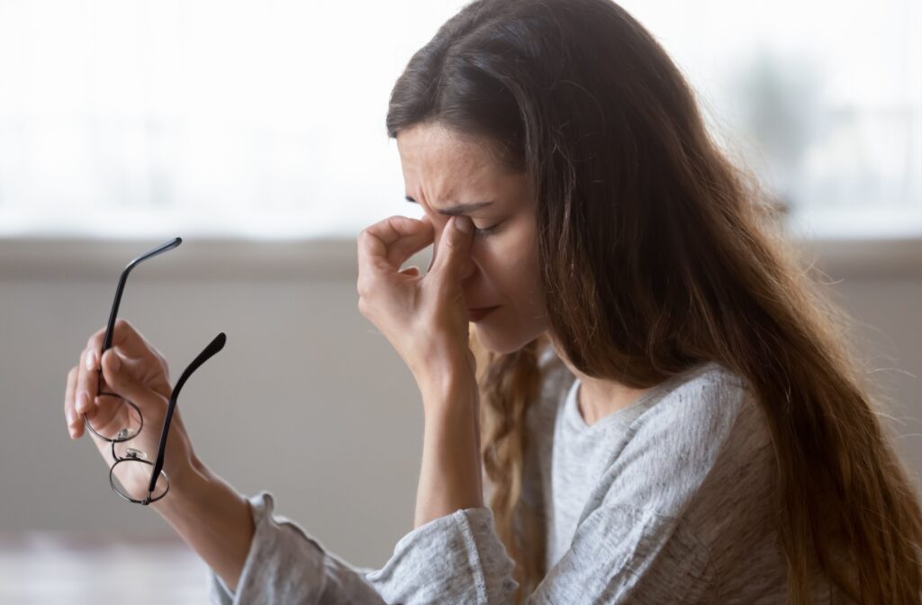 A young adult taking off their glasses in frustration to rub their eyes, trying to figure out if their symptoms are dry eye or allergies.