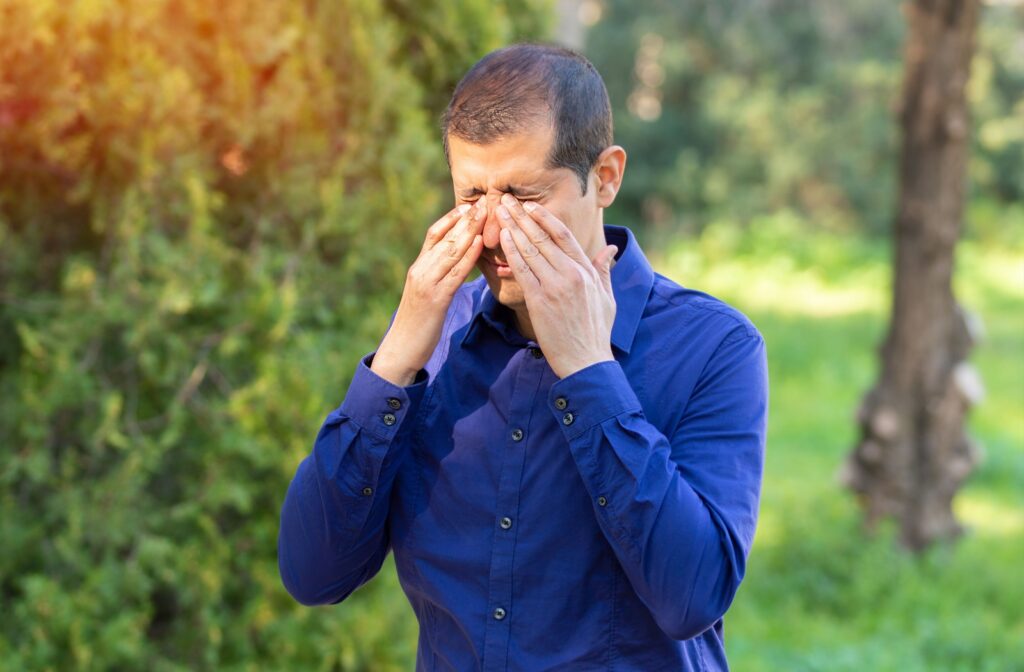 A person with dry eye disease rubs their eyes in discomfort while outdoors in the summer.