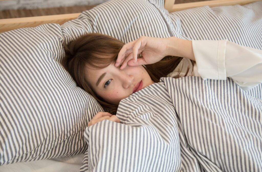 Person laying in bed rubbing their eye after waking up.