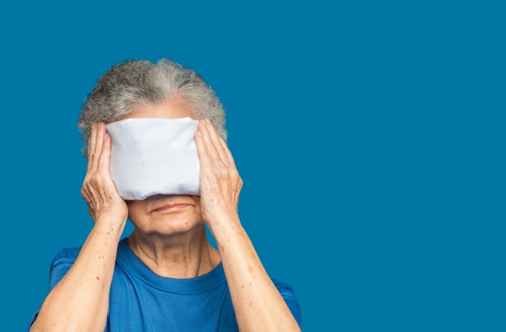 An older adult holds a warm compress on their eyes to alleviate dry eye symptoms from meibomian gland dysfunction.