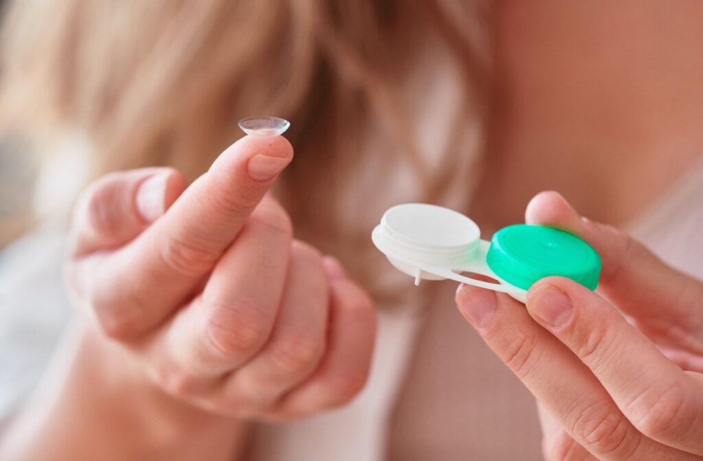 Close-up of someone holding a contact lens on their fingertip in one hand and a contact lens case in the other hand.