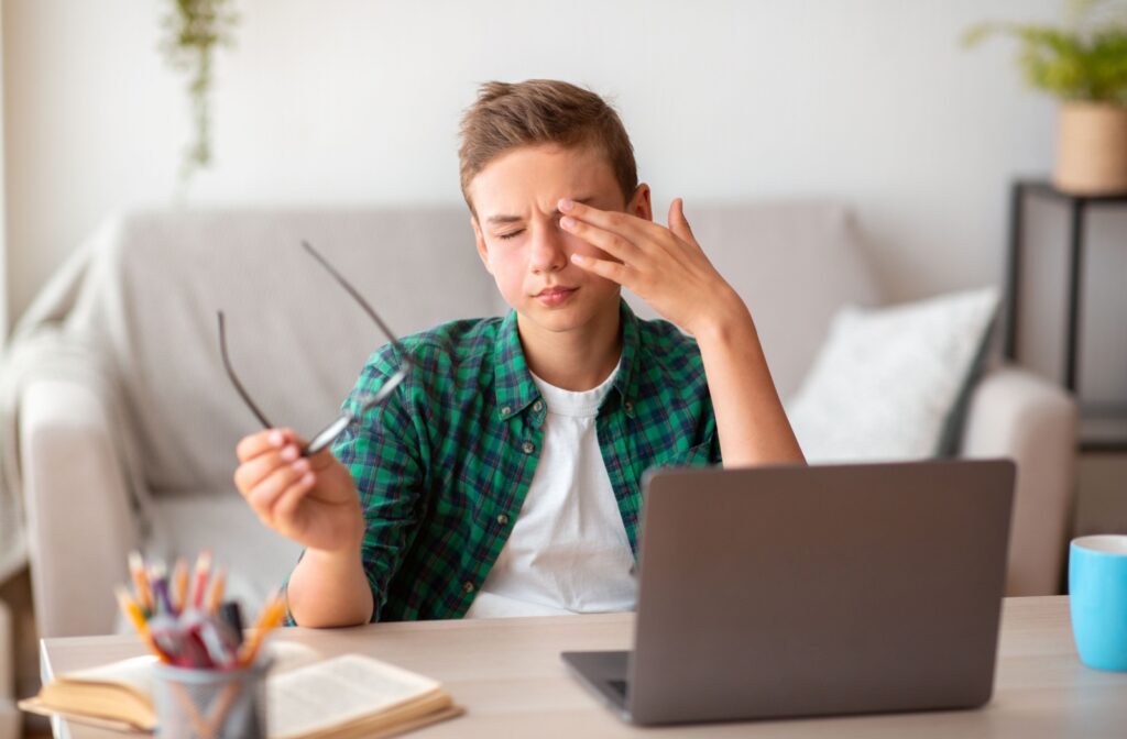 Teenage sitting in front of a computer holding their glasses so they can rub their eye